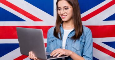 Młoda dziewczyna z laptopem w dłoni na tle flagi brytyjskiej.
