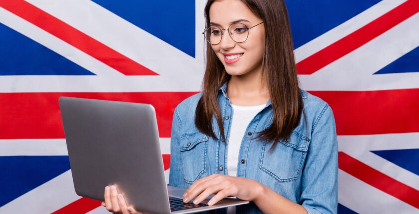 Młoda dziewczyna z laptopem w dłoni na tle flagi brytyjskiej.